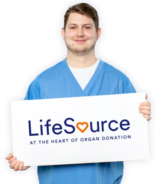 Young man wearing blue scrubs holding a sign that says LifeSource at the Heart of Organ Donation